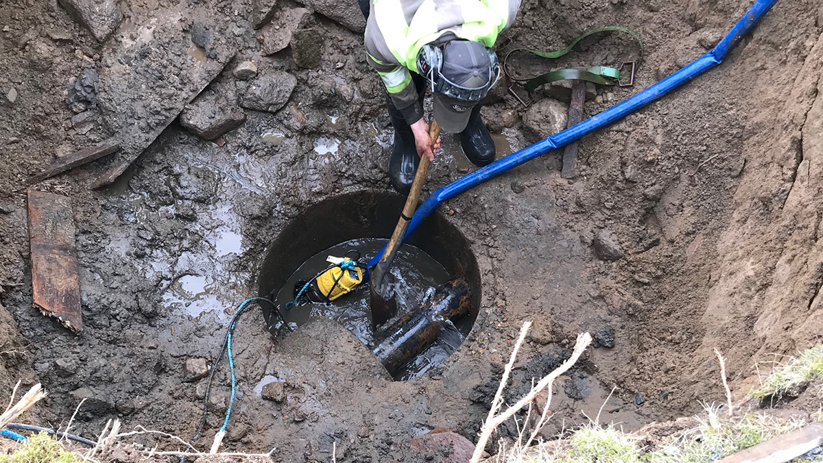 En man arbetar i en grävd grop där det finns en brunn med vatten. 