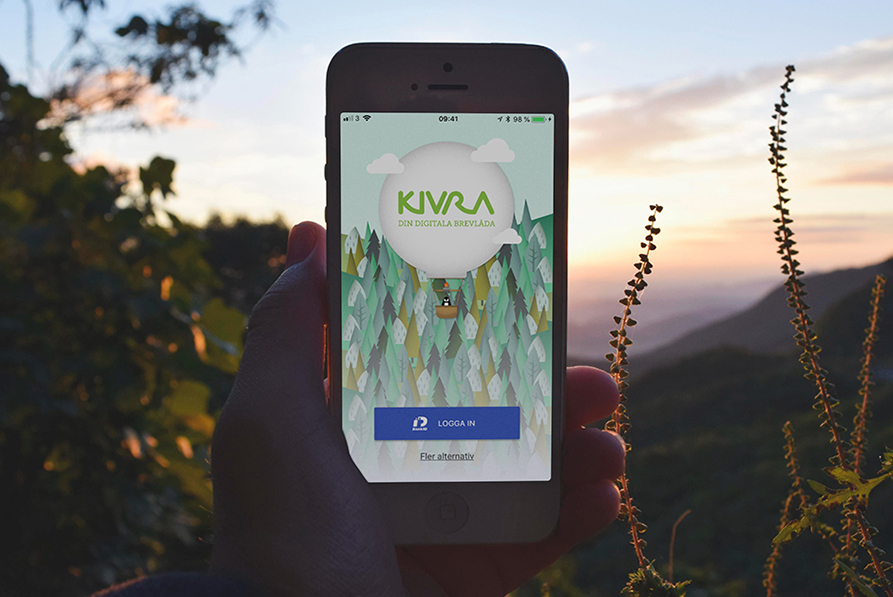 En persons hand håller en mobiltelefon. På telefonens skärm visas appen Kivra. Personen som håller telefonen är naturen och man ser berg, växter och en vacker himmel på bilden. 