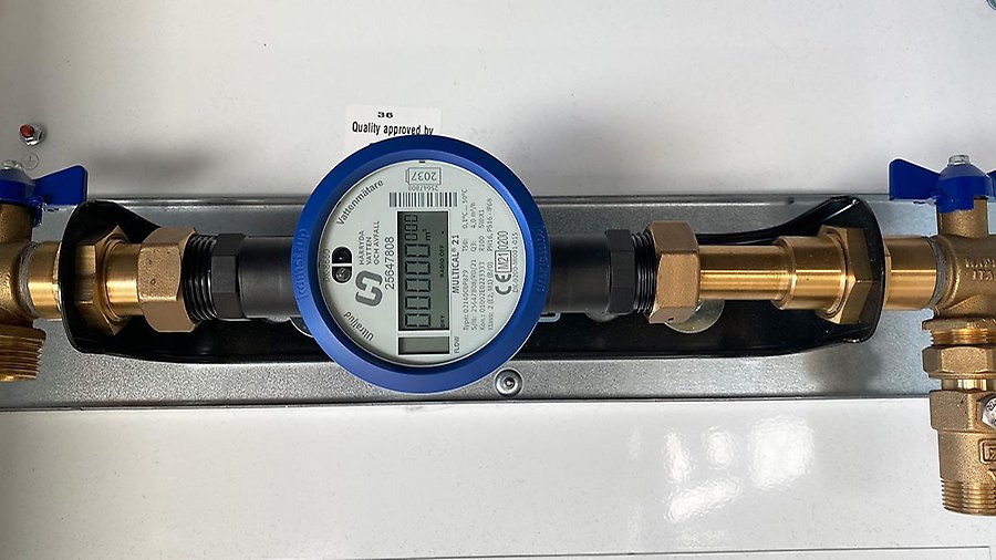 En vattenmätare sitter fast i ett väggfäste (konsol) som håller mätaren och rören med avstängningsventiler på plats. 