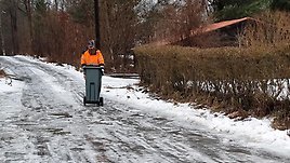 En man klädd i Renovas arbetskläder drar en soptunna på en isig och snötäckt väg. 
