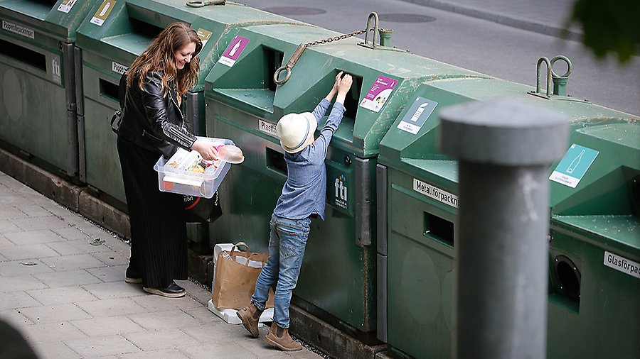 En kvinna och ett barn slänger förpackningar på en återvinningsstation. 