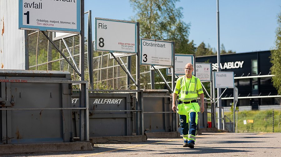 En man som arbetar på återvinningscentralen går bredvid containrar som man ska lägga avfall i. 