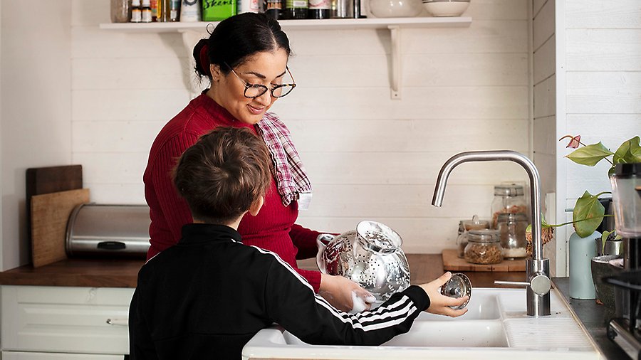 En kvinna diskar med rinnande vattenkran. En pojke visar henne proppen för att fylla diskhon istället. 