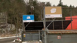 Nya skyltar med symboler i färg har satts upp ovanför två containers på återvinningscentralen. På en står det tidningar och på den andra skylten står det wellpapp. 